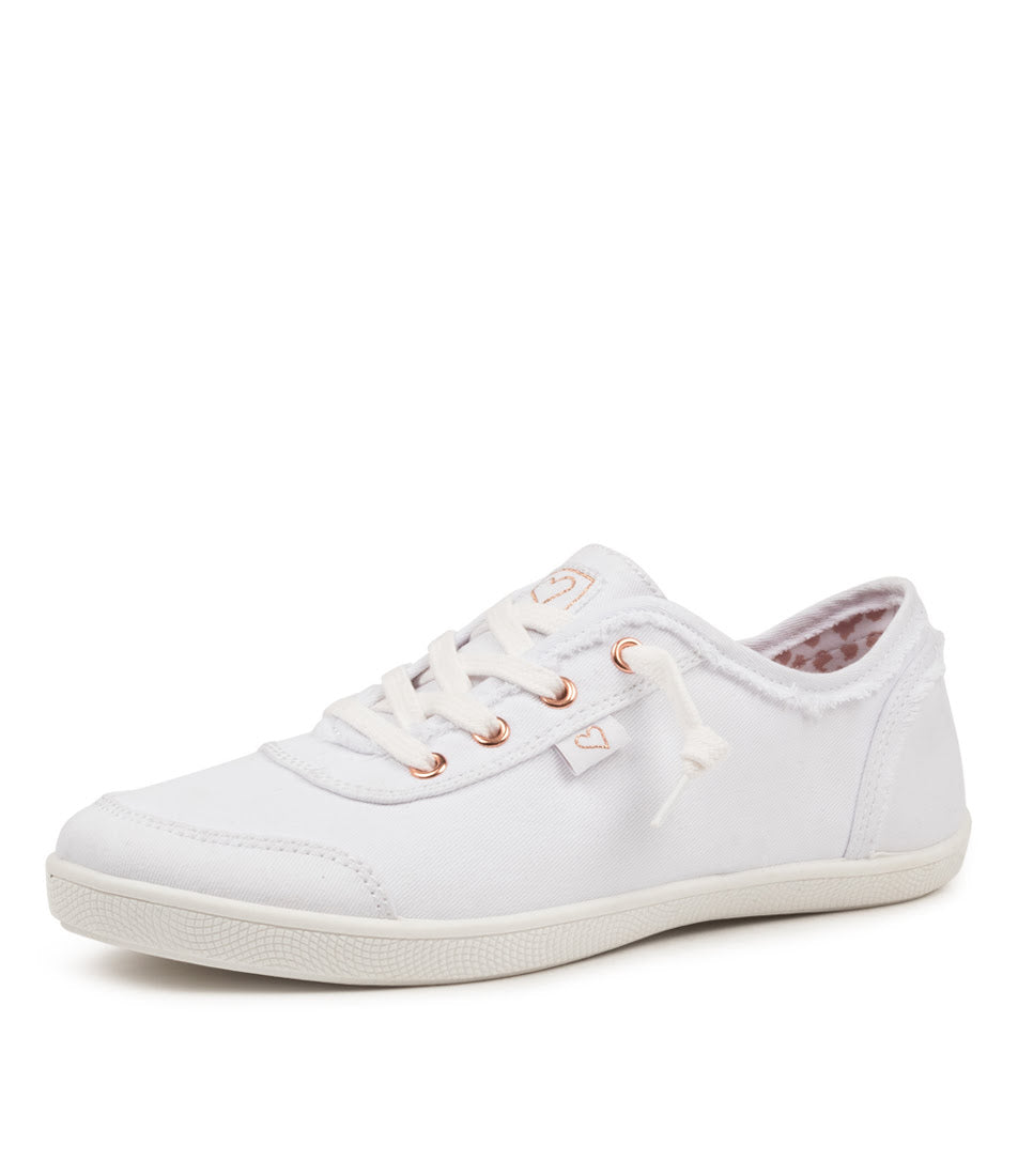 A white canvas low-top sneaker with white laces, rose gold eyelets, and a white rubber sole, shown from a side profile on a white background.